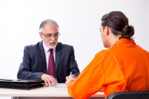 Man in prison jumpsuit sits across desk from criminal defense lawyer