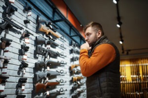 A man standing in front of a rack of guns, wondering if owning a gun is a civil right.
